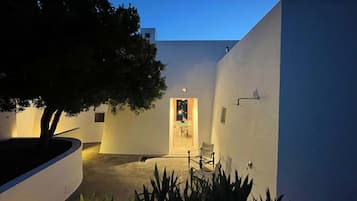 A modern building with a white exterior, a tree in the foreground, and a door leading to an interior space.