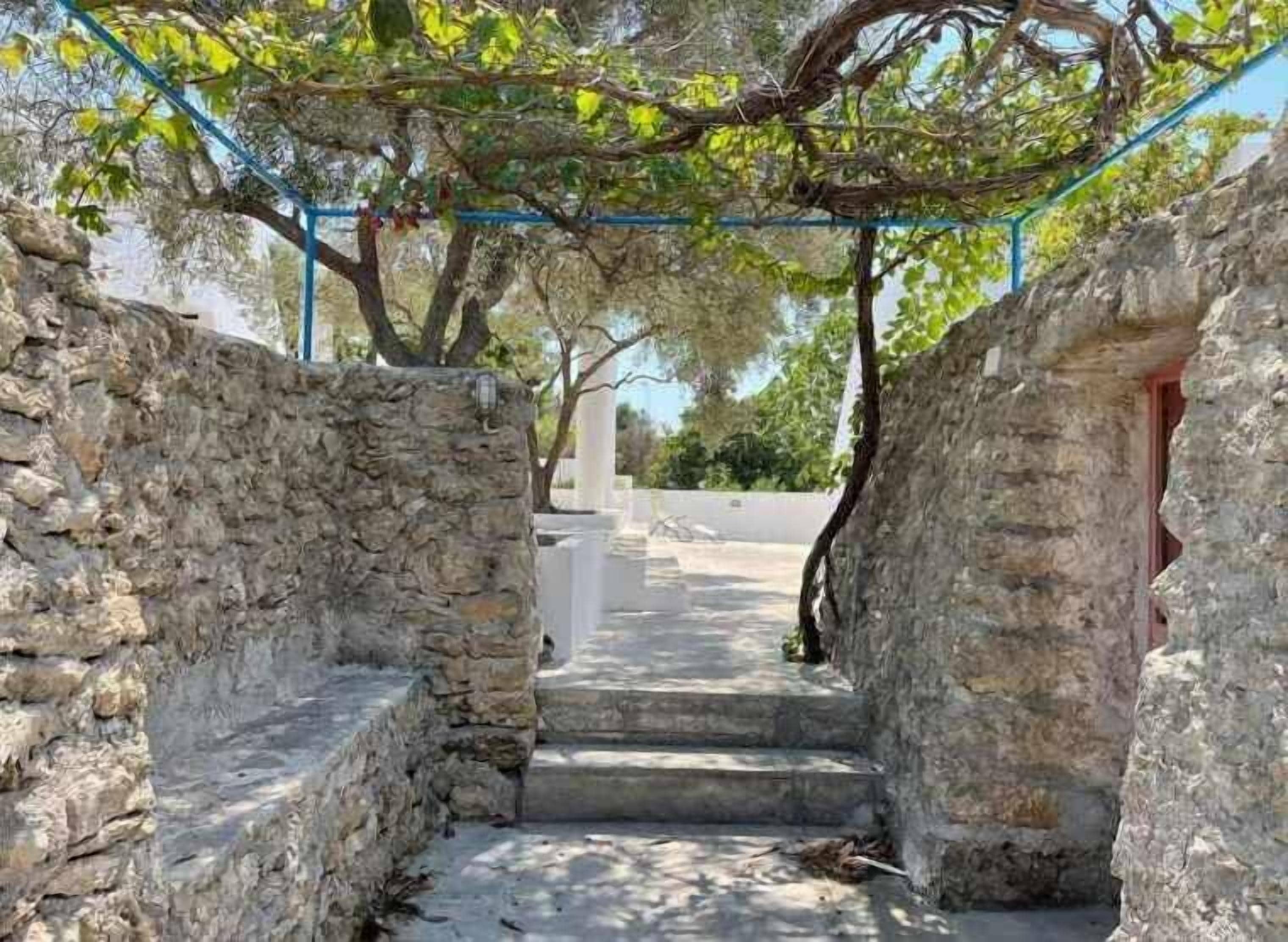 A stone pathway leading to a building entrance, surrounded by stone walls and trees.