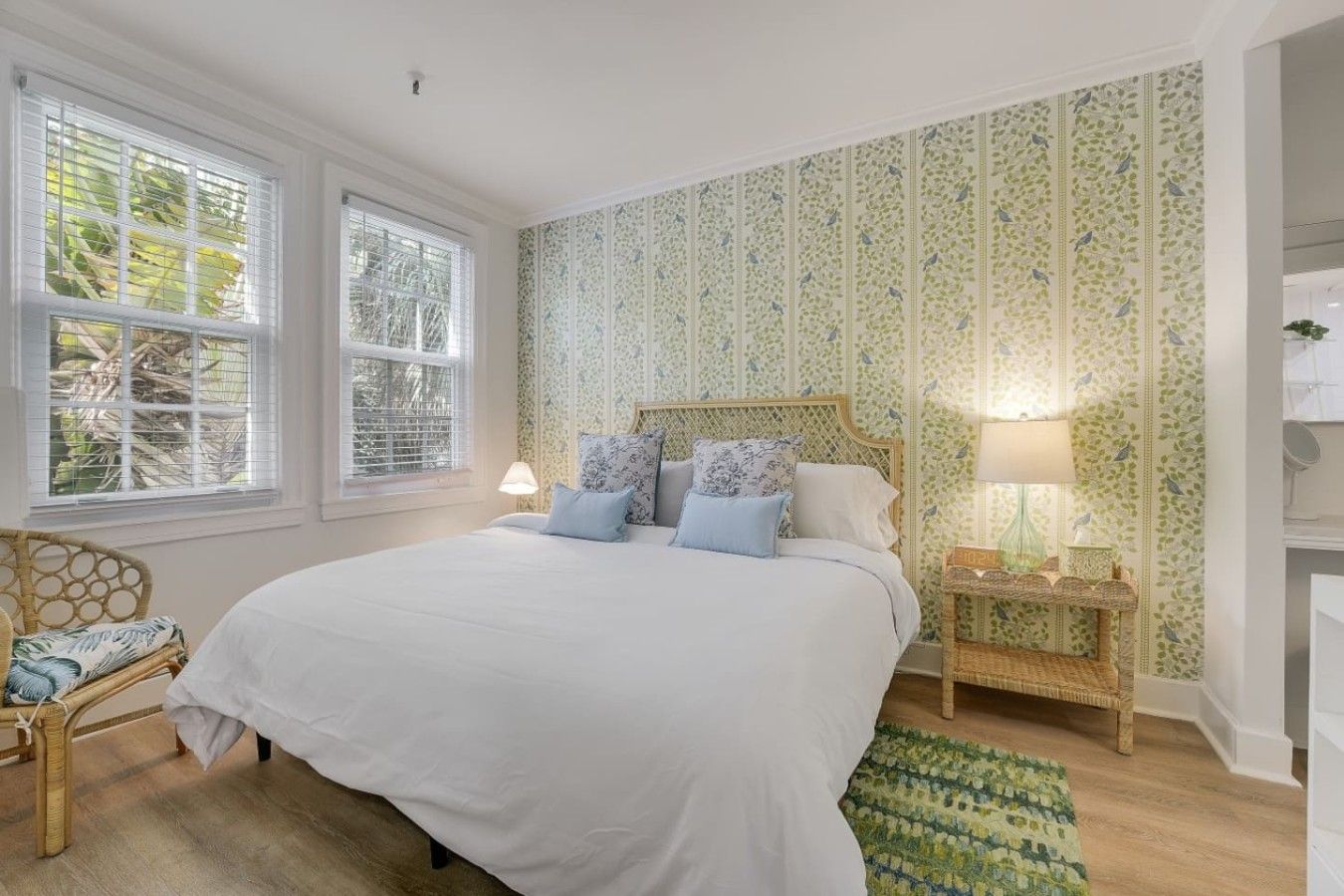 Une chambre avec un grand lit, deux lampes de chevet, un fauteuil en osier et un mur décoré d’un motif.