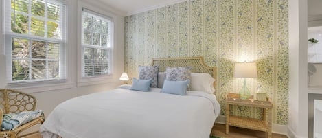 Une chambre avec un grand lit, deux lampes de chevet, un fauteuil en osier et un mur décoré d’un motif.