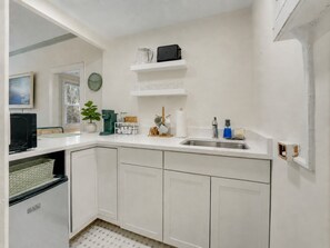A kitchen with white cabinets, a sink, a clock, and a coffee maker on the countertop. - The Atelier on the Island - Steps to Beach (Palm Beach)