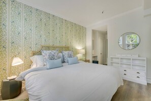Un dormitorio con una cama grande, una mesita de noche con lámpara, un aparador y un espejo en la pared.