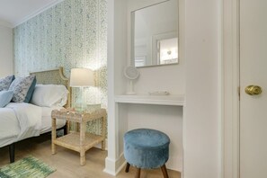 A bedroom with a bed, a bedside table with a lamp, a mirror, a small stool, and a wall-mounted shelf. - The Atelier on the Island - Steps to Beach (Palm Beach)