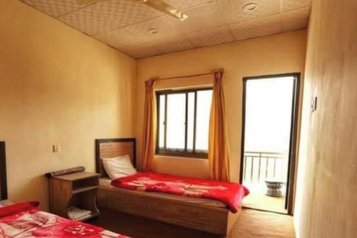 Una habitación con dos camas, una ventana con cortinas, una mesita de noche y vistas al exterior.