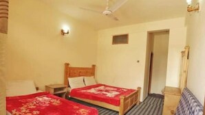 Un dormitorio con dos camas, un ventilador de techo, un ventanal pequeño y una puerta que da a otra habitación.