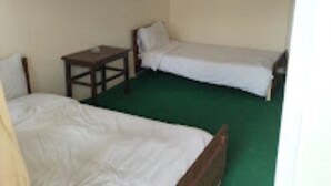 Una habitación pequeña con dos camas individuales, una mesita de noche de madera y una alfombra verde.