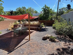 Eine Terrasse mit Tisch und Stühlen, einer Holzbank und einem roten Sonnensegel.