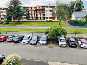 Un estacionamiento con varios coches, un edificio con balcones y un área verde al fondo.