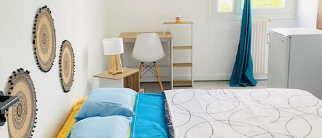 Une chambre à coucher avec un lit, un bureau, une chaise, une lampe et une fenêtre avec des rideaux.