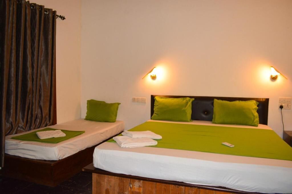 Two single beds with green bedding, a wooden headboard, and a wall-mounted light fixture.
