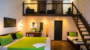 Quarto de hotel com uma cama, escrivaninha, cadeira, mesinha, espelho, porta e escada.