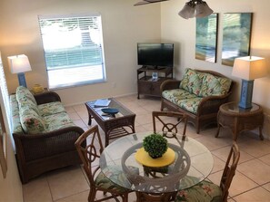 A living room with a television, wicker furniture, a glass coffee table, and a dining area with chairs and a small table. - Areas Best Value - Private - Near all attractions- Secure and Immaculately Clean (Nokomis)