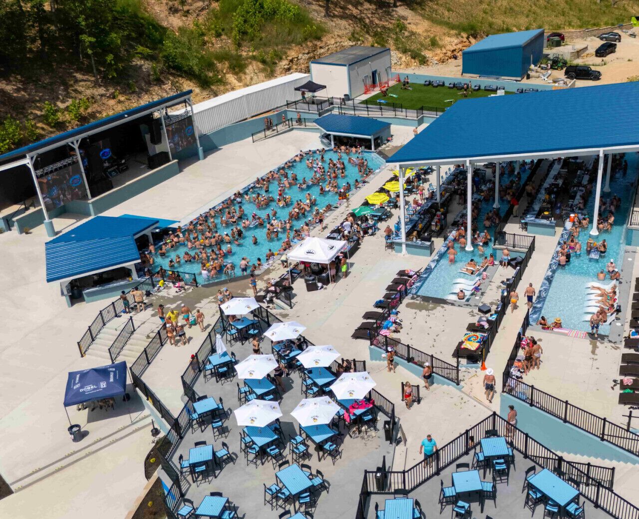 A large outdoor swimming pool area with multiple lanes, sun loungers, and shaded seating areas.