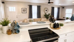 A modern kitchen with a built-in stove, white cabinetry, and a dining area with a sofa.