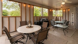 An outdoor patio with a round table, chairs, a grill, and a ceiling fan.
