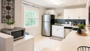 A modern kitchen with white cabinetry, stainless steel appliances, a window with a view, and a sign that reads 'THANKFUL grateful BLESSED.'