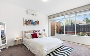 Ein Schlafzimmer mit Bett, Fenster, Klimaanlage, Wandbild und Nachttisch.