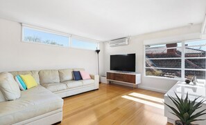 A modern living room with a sofa, TV, and large windows. - Large Bedroom with Courtyard Near St Kilda Beach (St Kilda)