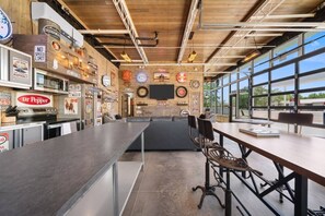 A bar area with a long counter, seating, and a large window. - Krusty`s Motor Suite | Historic Gas Station Converted Retro Neon Garage! (Hanksville)