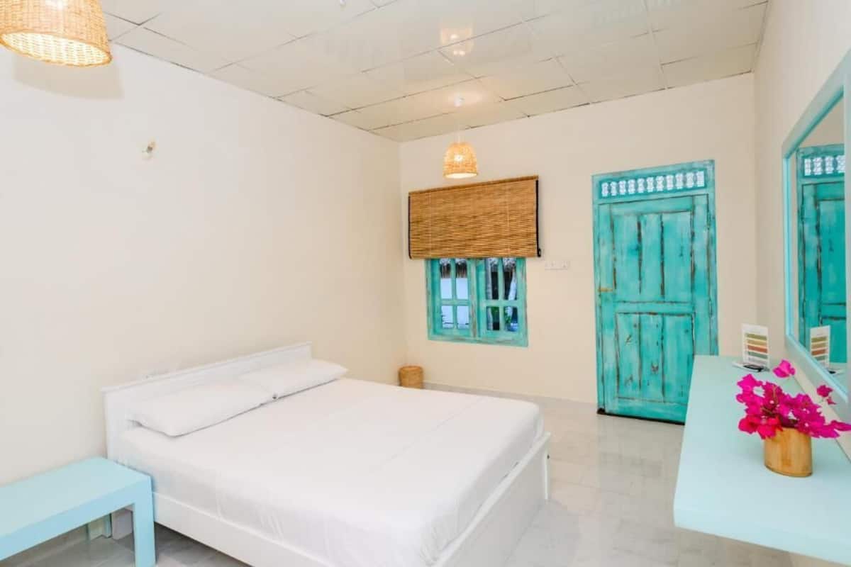 Un dormitorio con cama, mesita de noche, ventana con vistas y puerta.