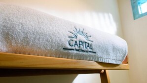 En vit handduk med broderade bokstäver som bildar orden ”CAPITAL” och ”Hotel Concourse”, placerad på en trästol.
