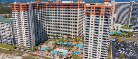 Ein Hochhaus-Hotel mit mehreren Balkonen, einem zentral gelegenen Pool und einer Strandanlage.