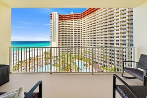 Un balcó amb vista a un edifici d'hotel, una piscina i una platja.