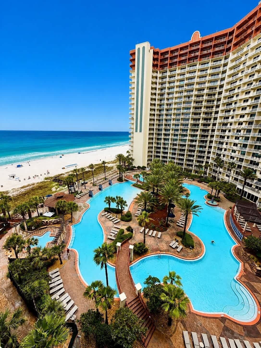 A resort with a large pool area, a beach, and a high-rise building.