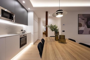 Eine moderne Küche mit integrierten Geräten, ein Essbereich mit Holztisch und eine große Pflanze.