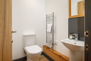 Ein kleines, modernes Badezimmer mit Toilette, Handtuchhalter, Waschbecken und Spiegel.