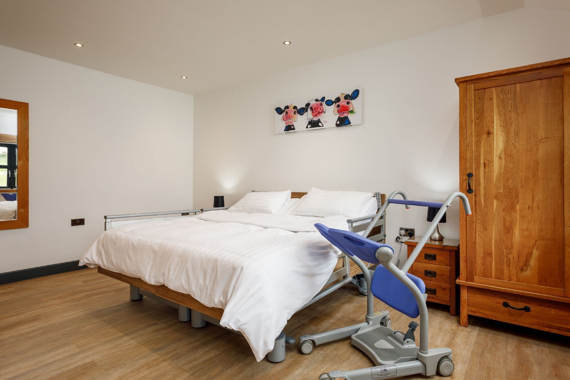 A hospital room with a bed, a wheelchair, a wooden cabinet, and a painting on the wall.