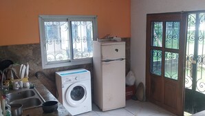 Eine Küche mit Waschmaschine, Kühlschrank, Spüle und einem Fenster mit dekorativen Eisengittern.