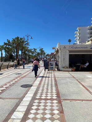A pedestrian walkway with a tiled pattern, palm trees, and a building with a sign reading 'Restaurante'. - Benalmadena Diana I Tourist Apartment (Benalmádena)