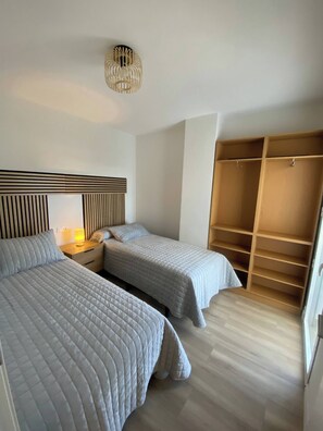 Et soveværelse med to senge, et natbord med lampe, et klædeskab og en hængende lampe.