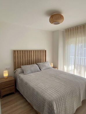A bedroom with a wooden headboard, a bed with a quilted bedspread, a bedside lamp, and a window with sheer curtains. - Benalmadena Diana I Tourist Apartment (Benalmádena)