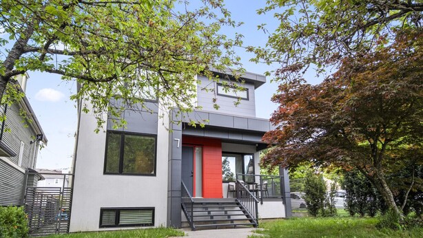 Ein modernes, zweistöckiges Haus mit roter Tür, einer zur Einfahrt führenden Treppe und einem umlaufenden Garten.