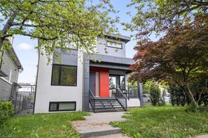 Una casa moderna de dos pisos con una puerta roja, una escalera que lleva a la entrada y un jardín circundante.