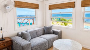 Una habitación con un sofá gris, una mesa redonda y ventanas con vistas a la playa y al océano.