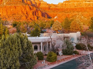 A residential area with a house featuring a front porch, a small garden with a birdbath, and a view of red rock formations in the background. - Angel View: Charming 3-bedroom 3bath house near Chapel of the Holy Cross, Sedona (Sedona)