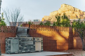 An outdoor kitchen with a grill and oven, a decorative wall, and a mountainous backdrop. - Angel View: Charming 3-bedroom 3bath house near Chapel of the Holy Cross, Sedona (Sedona)
