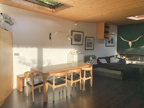 Un espace de vie moderne comprenant une table à manger en bois, des chaises, un canapé et une lampe fixée au mur.