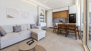 A modern living room with a sofa, a coffee table, and a dining area with chairs and a table. - Sea View Panorama | Green Coast 2BR Patio Retreat by PikHost (Palasë)