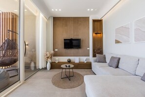Un salon moderne avec un canapé, une table basse, un téléviseur fixé à un mur en bois et une cloison en verre.
