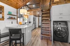 A kitchen with a central island, a washing machine, and a wooden staircase.