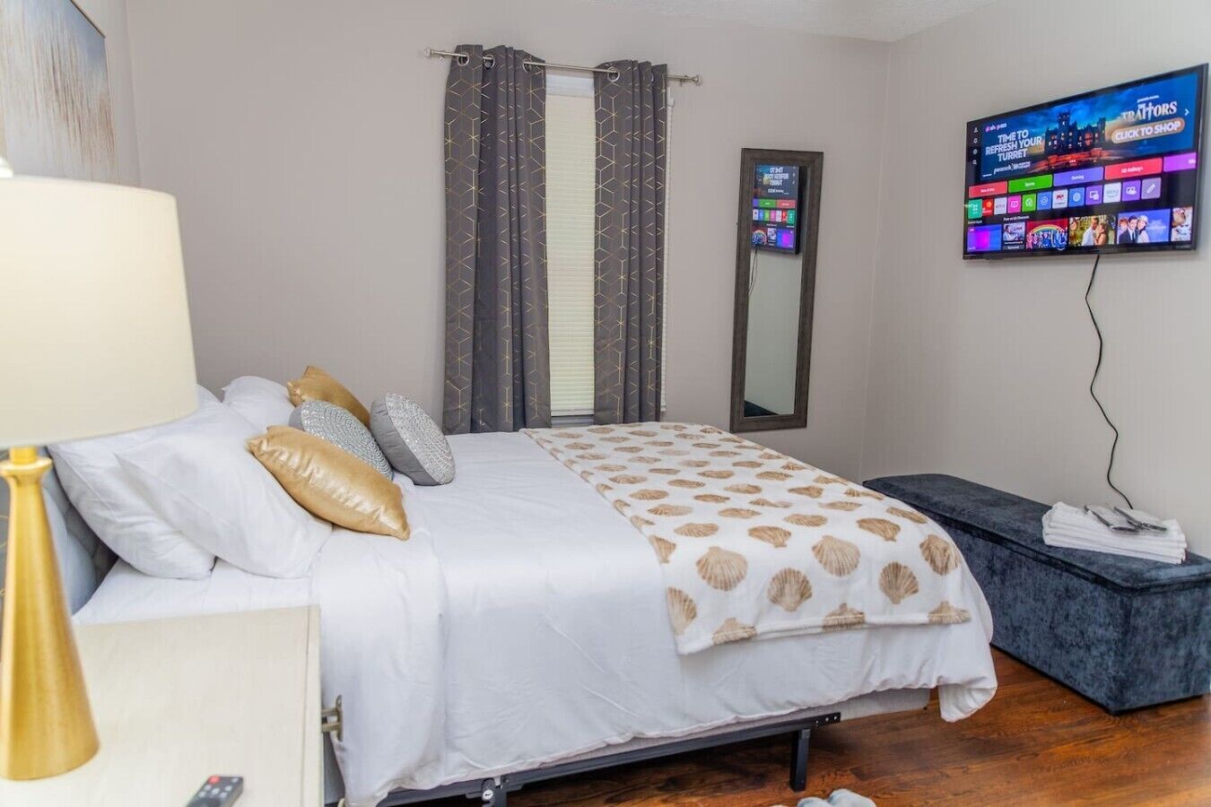 A hotel room with a bed, a TV, a mirror, and a bedside table.