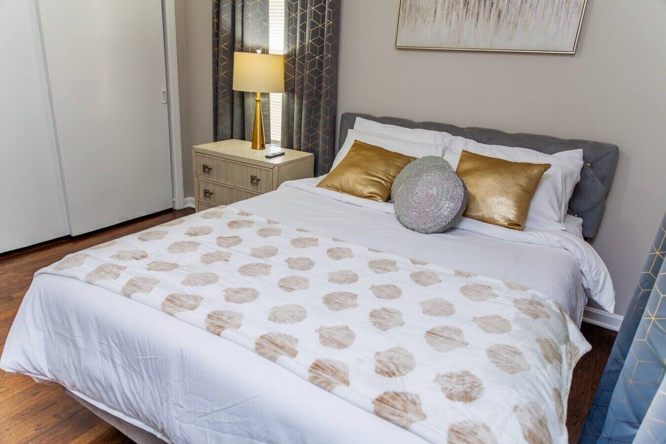 A neatly made bed with a patterned bedspread, a bedside table with a lamp, and a wall-mounted artwork.