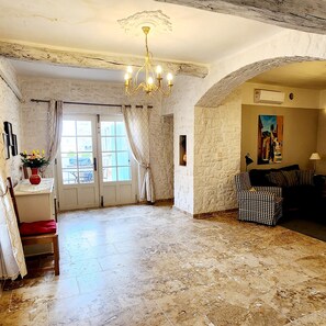 Ein geräumiges Zimmer mit einer Chandelier, einem karierten Sofa, einem Gemälde an der Wand und einer zur Außenwelt führenden Tür.