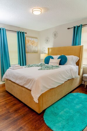 A neatly made bed with a headboard, a blue rug, and a painting on the wall. - Cozy Inside, All Things Outside (Decatur)
