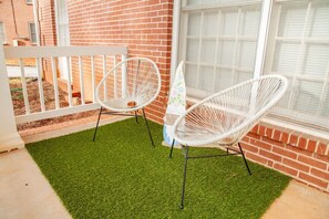 A patio with two white wicker chairs, a small table, and a decorative gnome statue. - Cozy Inside, All Things Outside (Decatur)