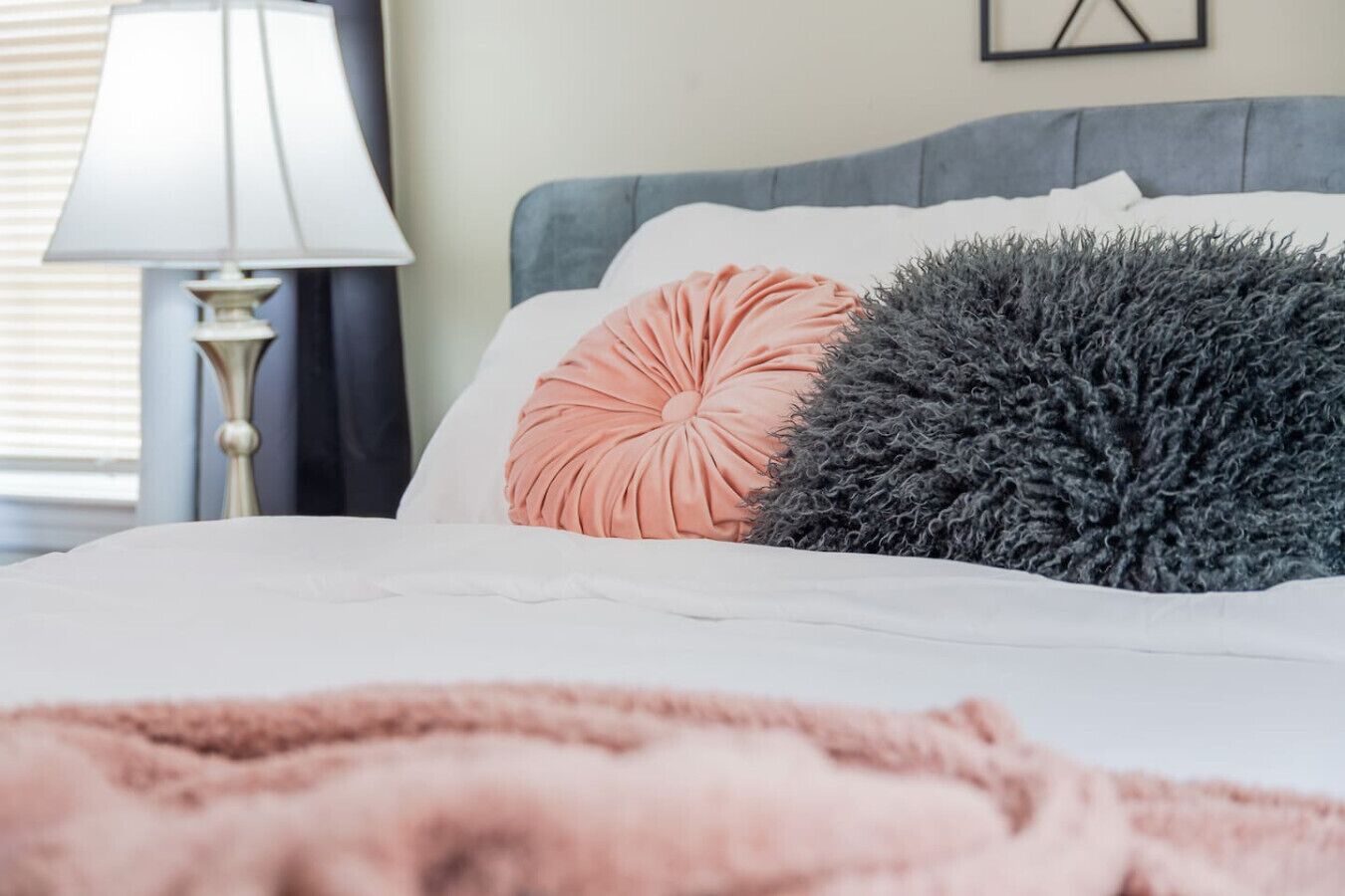 A bed with a white duvet, a peach-colored pillow, and a gray fluffy pillow.